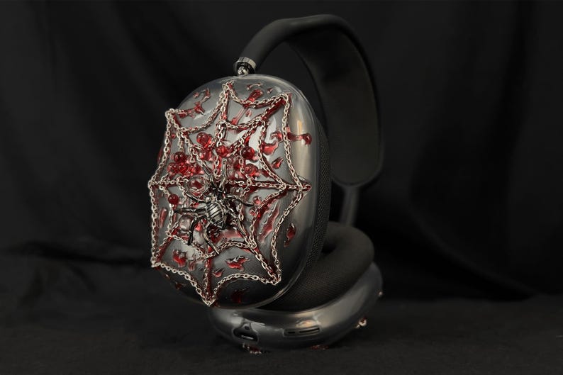 May include: Black headphones with a silver spider web design on one earcup. The web is decorated with red jewels and a silver spider.