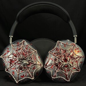 May include: Over-ear headphones with a black headband and silver earcups decorated with a red spiderweb design and silver spiders.