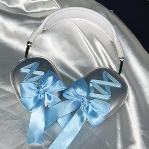 Puede incluir: Auriculares blancos con un lazo de sat&eacute;n azul claro en cada auricular. Los lazos est&aacute;n atados con un patr&oacute;n de cruz.