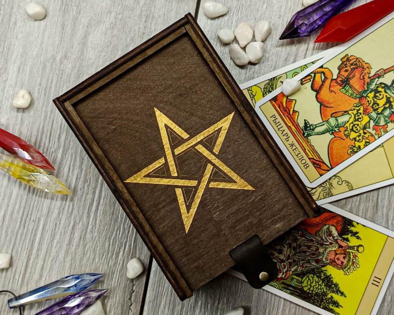 May include: A wooden box with a gold pentagram design on the lid. The box is surrounded by tarot cards, including the Knight of Wands and the Empress.