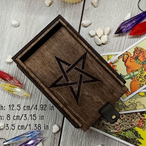 May include: A wooden box with a pentagram design on the lid. The box is 12.5 inches long, 8 inches wide, and 3.5 inches deep. It is made of dark wood and has a leather strap closure.