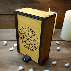 May include: A wooden box with a dark brown trim and a compass design engraved on the front. The compass design features runes and the letters "M.F.D.P.R.X.P.N.X.I.Z.F.M."