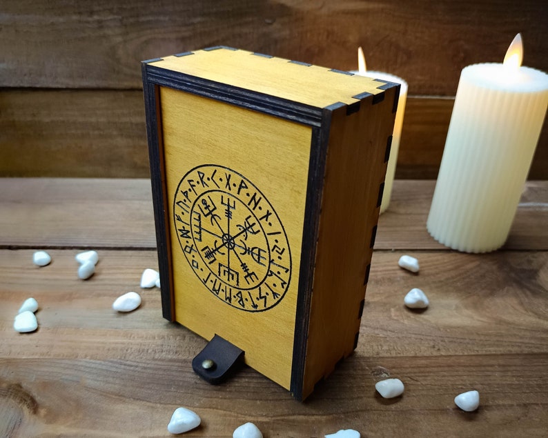 May include: A wooden box with a dark brown trim and a compass design engraved on the front. The compass design features runes and the letters "M.F.D.P.R.X.P.N.X.I.Z.F.M."