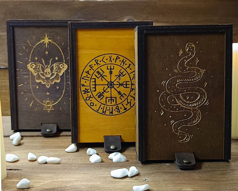 May include: Three wooden boxes with different designs. The first box has a butterfly design, the second box has a compass design with the text "X-PN-X", and the third box has a snake design.