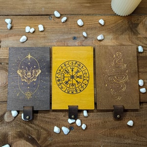 May include: Three wooden plaques with different designs. The first plaque has a butterfly with a skull in the center. The second plaque has a compass with the text "・N・P・F・R・<・X・P-N-X-". The third plaque has a snake with a tail that forms a circle.