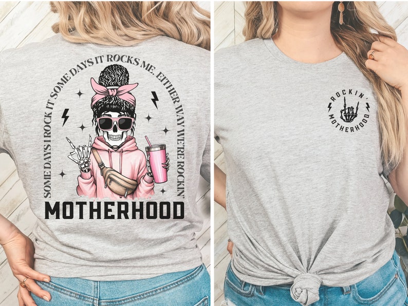 K&ouml;nnte beinhalten: Graues T-Shirt mit einem Skelett, das einen rosa Hoodie und eine Sonnenbrille tr&auml;gt. Der Text auf dem Shirt lautet "Some days I rock it some days it rocks me, either way we're rockin' motherhood". Die R&uuml;ckseite des Shirts hat eine Skeletthand mit einer Rock'n'Roll-Handgeste. Der Text auf der R&uuml;ckseite des Shirts lautet "Rockin' Motherhood".