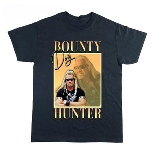 Pu&ograve; includere: Una maglietta nera con una grafica di Dog the Bounty Hunter. La grafica &egrave; in stile retr&ograve; con uno schema di colori giallo e arancione. Il testo "BOUNTY DOG HUNTER" &egrave; stampato in grandi caratteri grassetto.