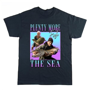 Puede incluir: Camiseta azul marino con un gráfico de dos hombres sosteniendo peces grandes. El texto "PLENTY MORE Fish IN THE SEA" se muestra en un degradado de azul, rosa y morado.