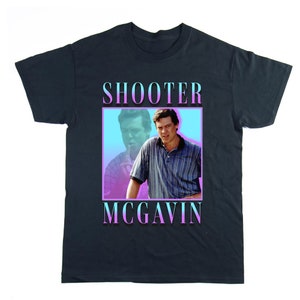 Puede incluir: Una camiseta azul oscuro con un gráfico retro de un hombre con el texto "Shooter McGavin" en un degradado rosa y azul.