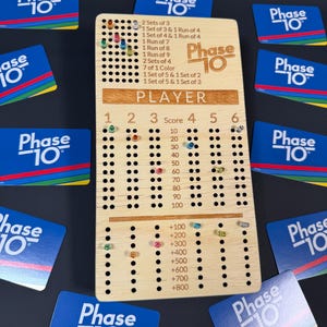Könnte beinhalten: Ein hölzernes Phase 10-Spiel-Scoreboard mit farbigen Stiften und Phase 10-Karten. Das Board hat Löcher zum Verfolgen von Spielständen und Phasen. Die Phase 10-Karten sind blau mit dem Logo des Spiels.