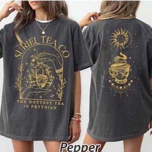 May include: A gray oversized t-shirt with a graphic print of a teacup, stars, and the text "SURIEL TEA CO. THE HOTTEST TEA IN PRYTHIAN". The back of the shirt has a graphic print of a teacup, a sun, a moon, and stars.