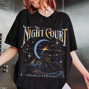 Op de afbeelding: Zwart T-shirt met een grafische print van een halve maan, sterren en bergen. De tekst "The Night Court" en "Velaris-City of Starlight" staat op het T-shirt gedrukt.