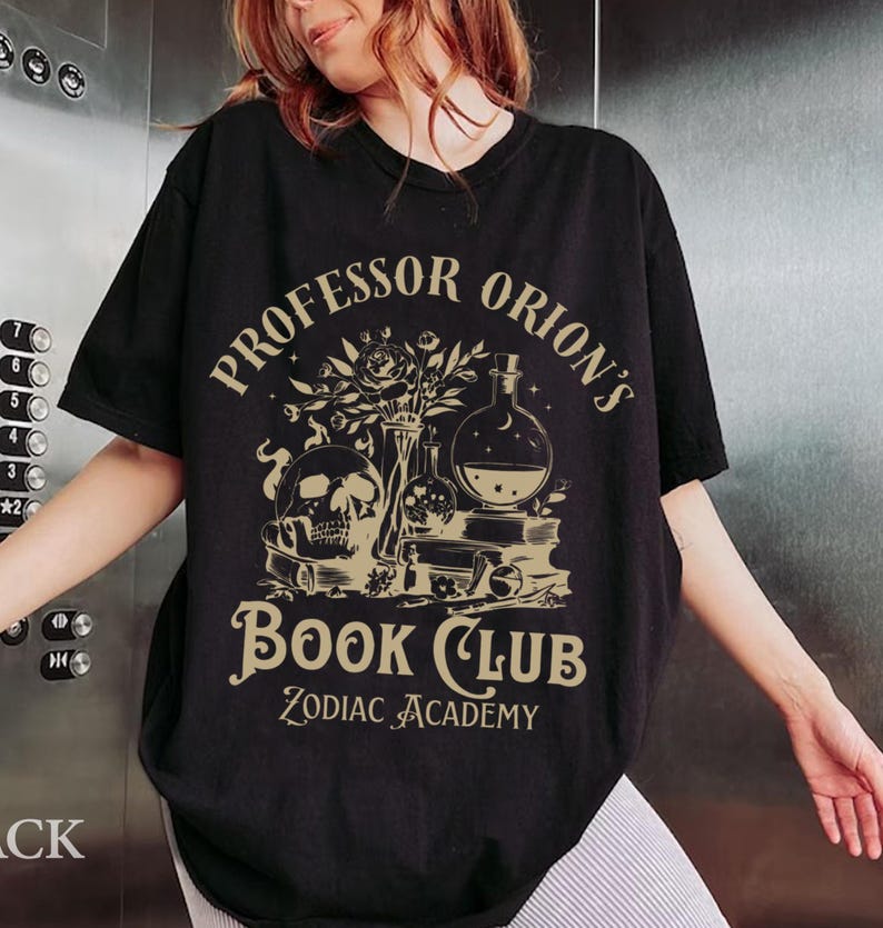 May include: Black t-shirt with a gold graphic design featuring a skull, flowers, and potion bottles. The text reads "Professor Orion's Book Club Zodiac Academy".