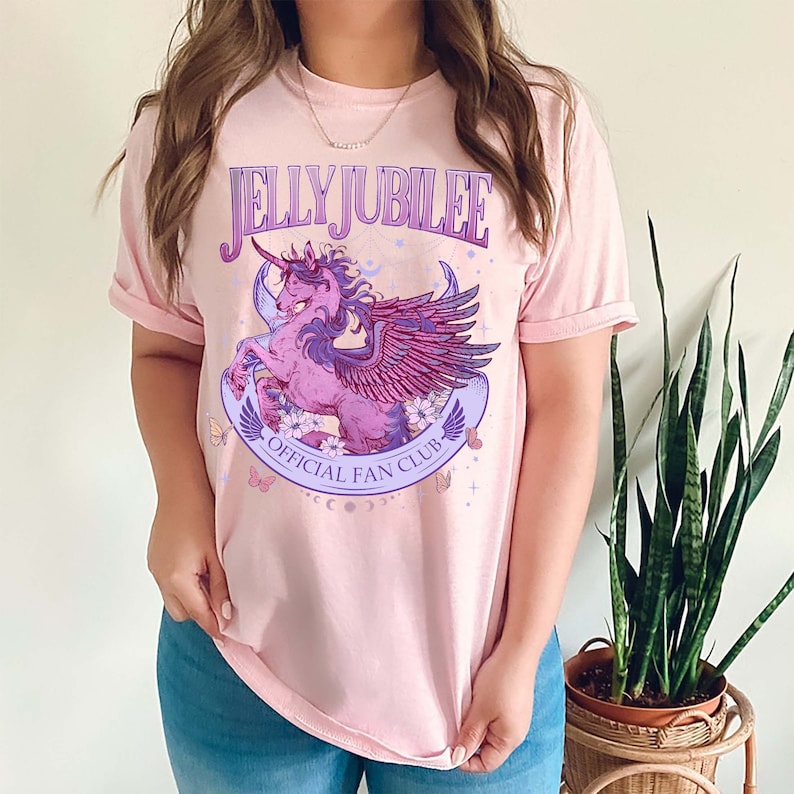 May include: A pink t-shirt with a graphic of a purple winged unicorn with the text "Jelly Jubilee Official Fan Club" printed on the front.