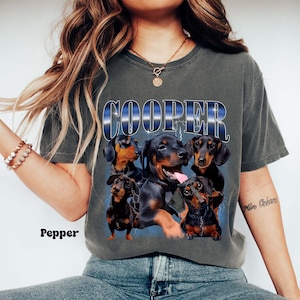 May include: A dark gray t-shirt with a graphic of five dachshund dogs. The dogs are black and brown and are arranged in a circle around the word "COOPER".