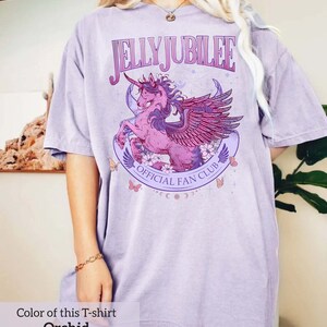 May include: A lavender colored t-shirt with a graphic of a winged unicorn with the text "Jelly Jubilee Official Fan Club".