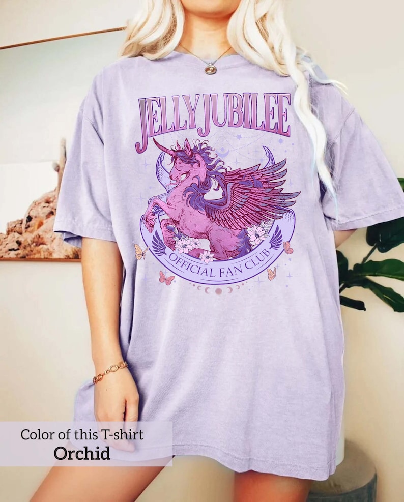 May include: A lavender colored t-shirt with a graphic of a winged unicorn with the text "Jelly Jubilee Official Fan Club".