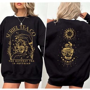 May include: Black sweatshirt with a gold design featuring a teacup, hands, and the text "Suriel Tea Co. The Hottest Tea in Prythian". The back of the sweatshirt has a gold design of a teacup with a sun and moon.