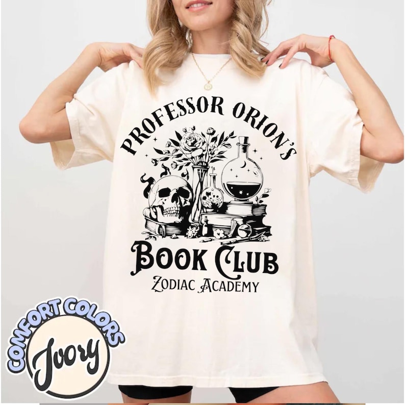 May include: A white t-shirt with a black graphic design that says "Professor Orion's Book Club Zodiac Academy". The graphic includes a skull, flowers, and a potion bottle.