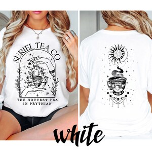 May include: White t-shirt with a black and white graphic design featuring a teacup, hands, and the text "Suriel Tea Co. The Hottest Tea in Prythian."