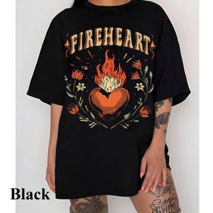Puede incluir: Camiseta negra de gran tama&ntilde;o con un estampado gr&aacute;fico de un coraz&oacute;n en llamas rodeado de flores y el texto "FIREHEART".