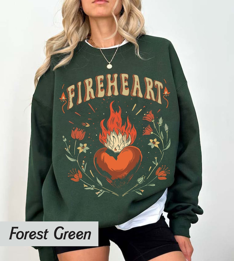 Puede incluir: Sudadera verde bosque con un estampado gr&aacute;fico de un coraz&oacute;n en llamas rodeado de flores y el texto "FIREHEART".