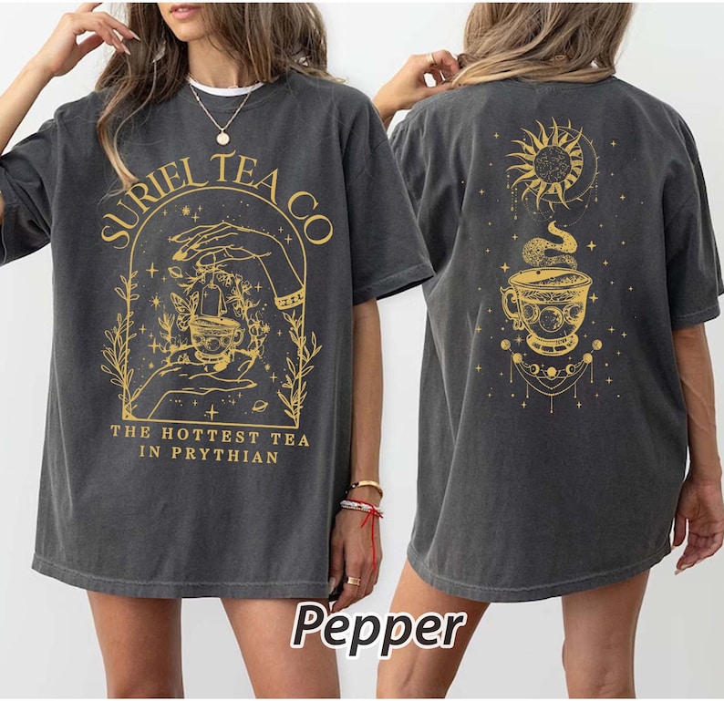 May include: A gray oversized t-shirt with a graphic print of a teacup, stars, and the text "SURIEL TEA CO. THE HOTTEST TEA IN PRYTHIAN". The back of the shirt has a graphic print of a teacup, a sun, a moon, and stars.