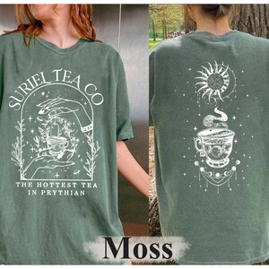 May include: A green t-shirt with a white graphic design featuring a teacup, stars, and the text "Suriel Tea Co. The Hottest Tea in Prythian".