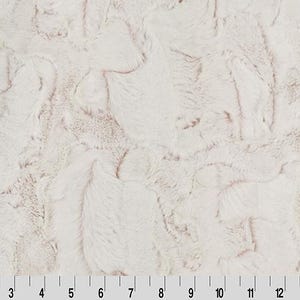 Könnte beinhalten: Nahaufnahme eines cremefarbenen Kunstfellstoffs mit einem strukturierten, gewirbelten Muster. Der Stoff hat ein weiches, plüschiges Aussehen mit subtilen Farbvariationen. Ein Lineal befindet sich am unteren Rand und zeigt Zollmessungen.