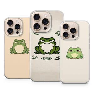 May include: Three phone cases with a cartoon frog design. The frogs are green and white with various expressions. The cases are beige and white with a clear border.