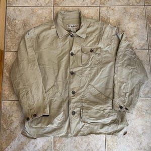 Peut inclure: Une veste boutonnée beige dotée d'un col pointu, d'une poche poitrine unique avec fermeture à bouton et de deux grandes poches plaquées inférieures. La veste présente des manches longues avec poignets boutonnés et une patte de boutonnage centrale.