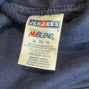 May include: A dark navy blue hooded sweatshirt featuring a white fabric tag with the Jerzees NuBlend logo. The tag indicates a size XL and a material composition of 50% cotton and 50% polyester, with manufacturing origin in El Salvador.