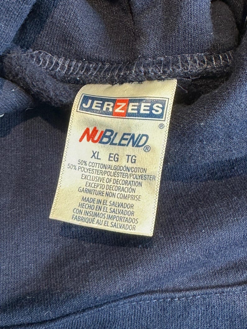 May include: A dark navy blue hooded sweatshirt featuring a white fabric tag with the Jerzees NuBlend logo. The tag indicates a size XL and a material composition of 50% cotton and 50% polyester, with manufacturing origin in El Salvador.