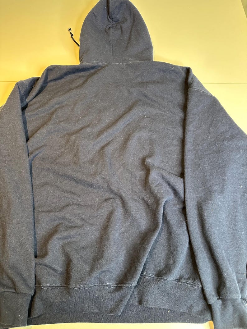 May include: A solid dark navy blue long-sleeve hooded sweatshirt featuring a drawstring hood, long sleeves with ribbed cuffs, and a ribbed hem. The garment is displayed from the back, showing a plain, unadorned fabric surface throughout the entire piece.