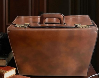 May include: A brown leather doctor's bag with a handle and brass clasps. The bag is open, revealing a dark interior. Beside the bag are brown leather gloves, a stethoscope, and books. The bag is on a wooden surface.