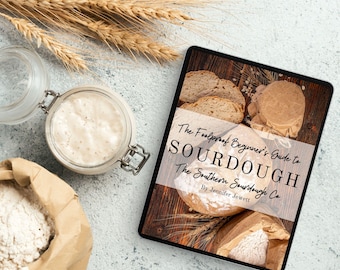 May include: A digital book cover with a rustic wood background. The title is "The Foolproof Beginner's Guide to Sourdough: The Southern Sourdough Co." by Jennifer Jewett. The cover features a close-up of freshly baked sourdough bread.
