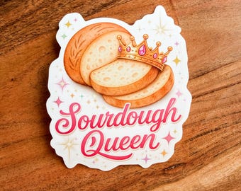 May include: A sticker featuring a loaf of bread and slices, topped with a gold crown with pink gems. The text "Sourdough Queen" is written in a cursive font with a pink outline. The sticker has a white border with star accents.