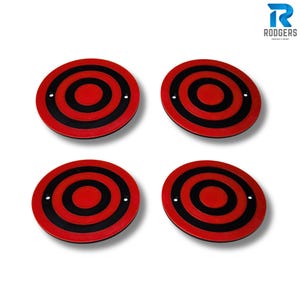 May include: Four circular coasters with a red and black bullseye design. Each coaster features a red centre, black concentric rings, and two small white dots. The coasters are displayed on a white background.