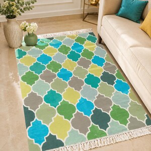 May include: A rectangular area rug featuring a repeating quatrefoil pattern in shades of bright blue, lime green, forest green, and grey. The rug has a white fringe along the two shorter ends and is laid out flat on a light-coloured floor.