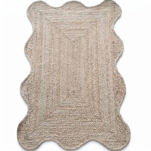 May include: A rectangular rug crafted from natural tan braided jute fibres. The rug features a distinct scalloped edge design along all four sides, creating a wavy border that frames the central rectangular woven pattern of the floor covering.