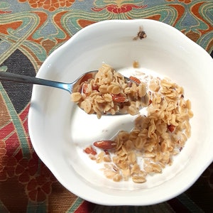 May include: A white bowl filled with a breakfast cereal with milk and almonds. A spoon is holding a portion of the cereal over the bowl.