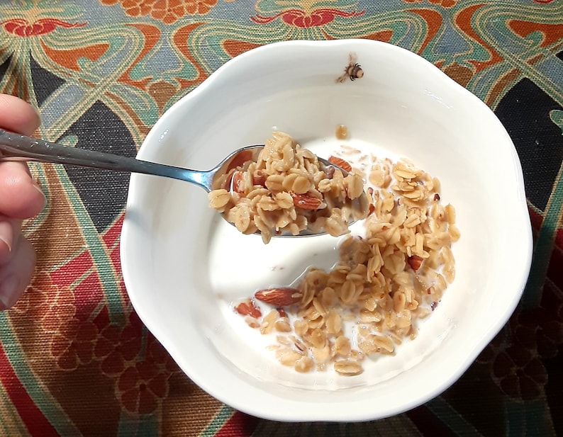 May include: A white bowl filled with a breakfast cereal with milk and almonds. A spoon is holding a portion of the cereal over the bowl.
