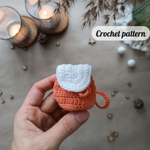 May include: A small crocheted orange backpack with a white crocheted flap. The backpack has a single strap.