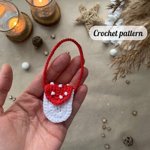 May include: A small crocheted purse shaped like a mushroom with a red top and white dots and a white bottom. The purse has a white crocheted strap.