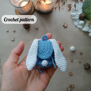 May include: A crocheted blue backpack with white bunny ears. The backpack has a white pom-pom on the front.