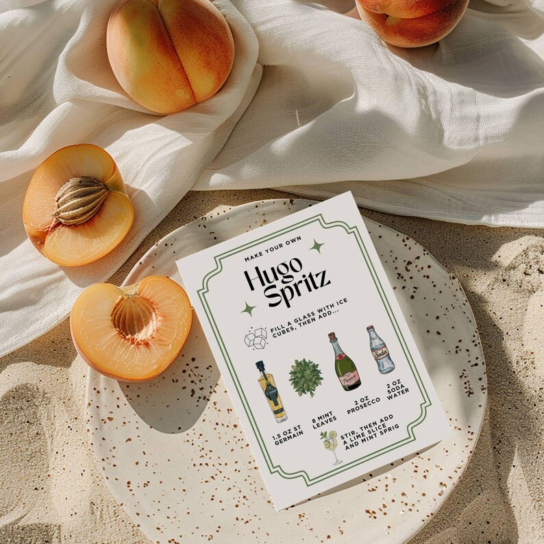 May include: A still-life image featuring a Hugo Spritz recipe card, peaches, and a plate. The recipe card lists ingredients like St. Germain, Prosecco, and soda water. Halved peaches with visible pits are arranged around the plate, with a white cloth in the background.
