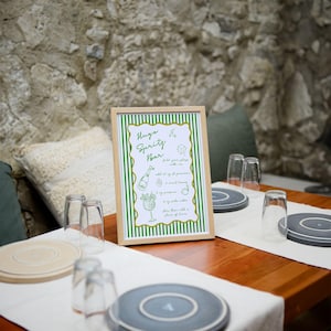 May include: A framed sign with green and white stripes that reads "Hygge Spritz Bar" with instructions for making a drink. The sign is on a wooden table with glasses and coasters.