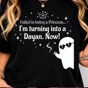 Peut inclure: Un t-shirt noir avec le texte blanc "Failed in being a Princess... I'm turning into a Dayan. Now!" accompagné d'un graphique représentant un fantôme portant des lunettes de soleil en forme de cœur et fumant, entouré de petites étoiles blanches.