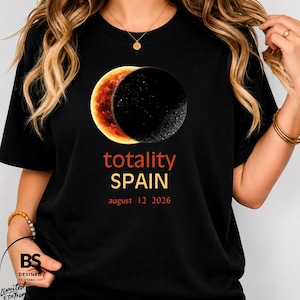 Op de afbeelding: Een zwart t-shirt met een afbeelding van een zonsverduistering met een gloeiende oranje sikkel en een donkere maan. Onder de afbeelding staat de tekst: totality SPAIN august 12 2026. Het ontwerp is gecentreerd op de borst van het kledingstuk.