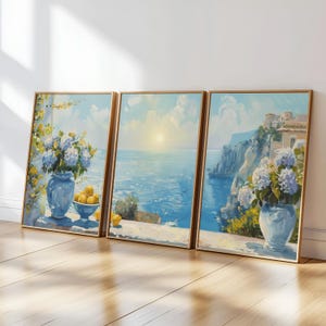 May include: Three framed landscape paintings depict a coastal scene with a bright sun over the sea. Each painting features a blue vase with white and blue flowers, and a bowl of lemons. The frames are a warm, light brown.